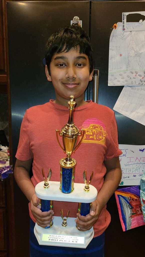 A boy holding two trophies after receiving chess coaching classes.