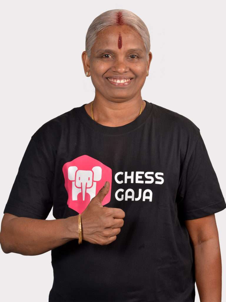 A woman giving a thumbs up in a black t-shirt with the words "chess for beginners" gala on it.