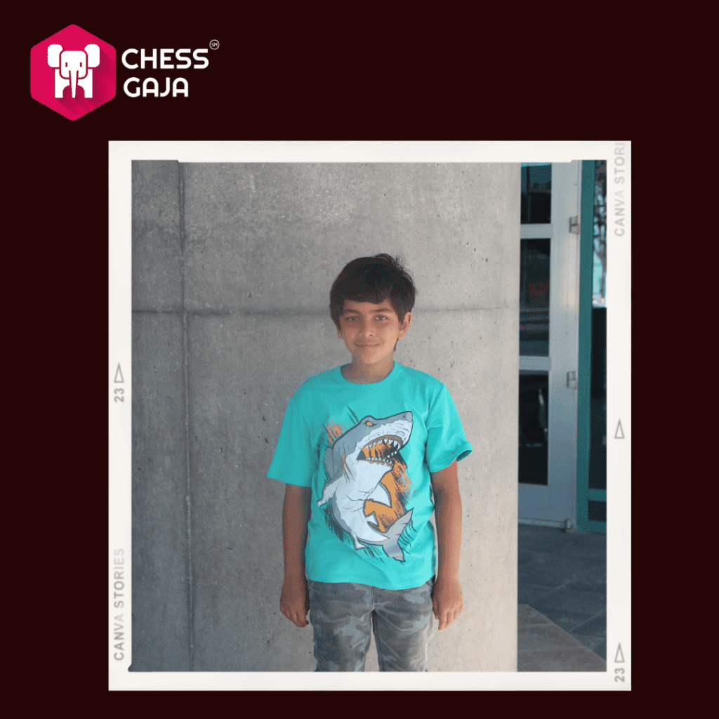 Young boy in a turquoise T-shirt with a chess design, standing in front of a gray concrete pillar.