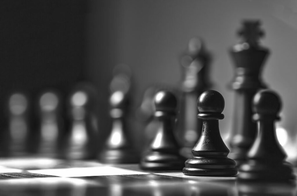 Black chess pawn and king pieces in moody black and white lighting, representing endgame technique