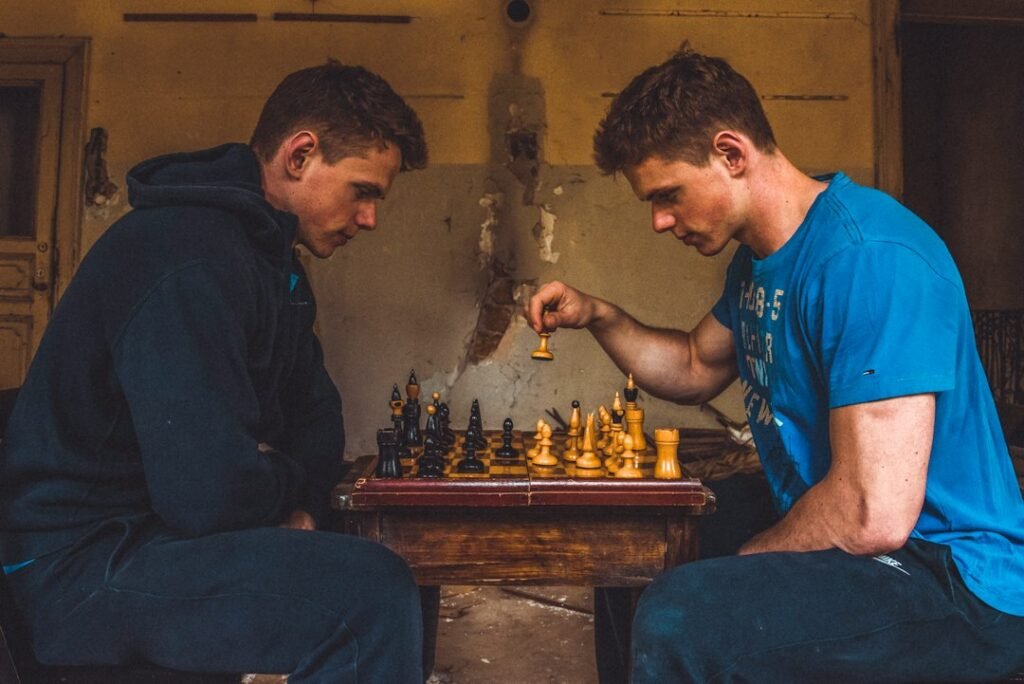 Two young men leaning intently over a chess board during a competitive match, illustrating the focused calculation required to see three moves ahead.