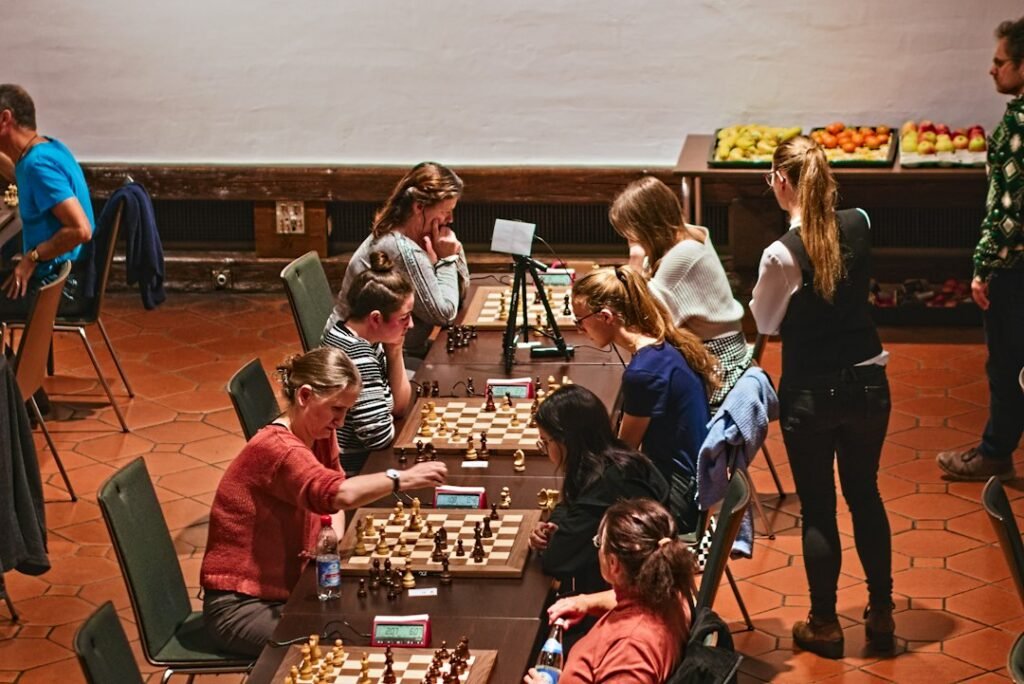 Group of young players competing at chess tournament tables with coaches observing