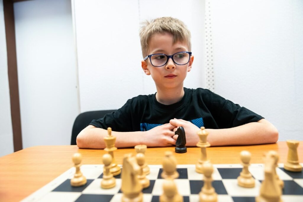 Young boy with glasses focused on a chess board, representing a competitive youth chess player working to break the 1200 rating barrier. Photo by Unsplash.